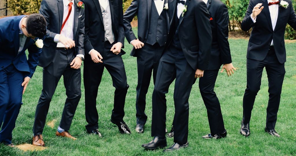 A group of young men all dressed up in suits having fun dancing on a grass