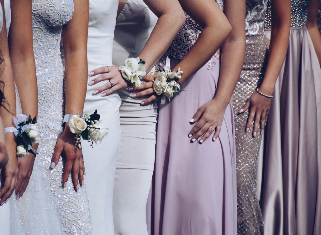 Young girls dressed in formal pastel colored gowns lined up for a picture wearing prom corsages